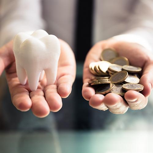 Person holding a model tooth in one hand and a number of coins in another